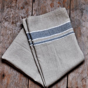 May include: Two linen tea towels with a blue and white striped border. The towels are folded and stacked on top of each other.