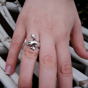 May include: A silver ring shaped like a gecko lizard. The ring is worn on a person's finger.