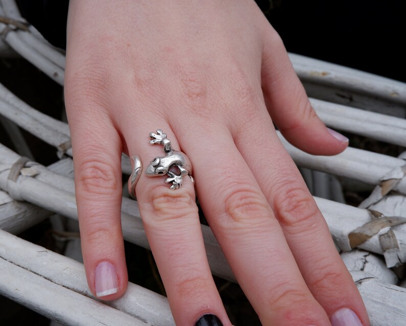 May include: A silver ring shaped like a gecko lizard with its tail wrapped around the finger.