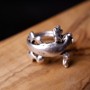 May include: A silver ring with a detailed design of a frog riding another frog.