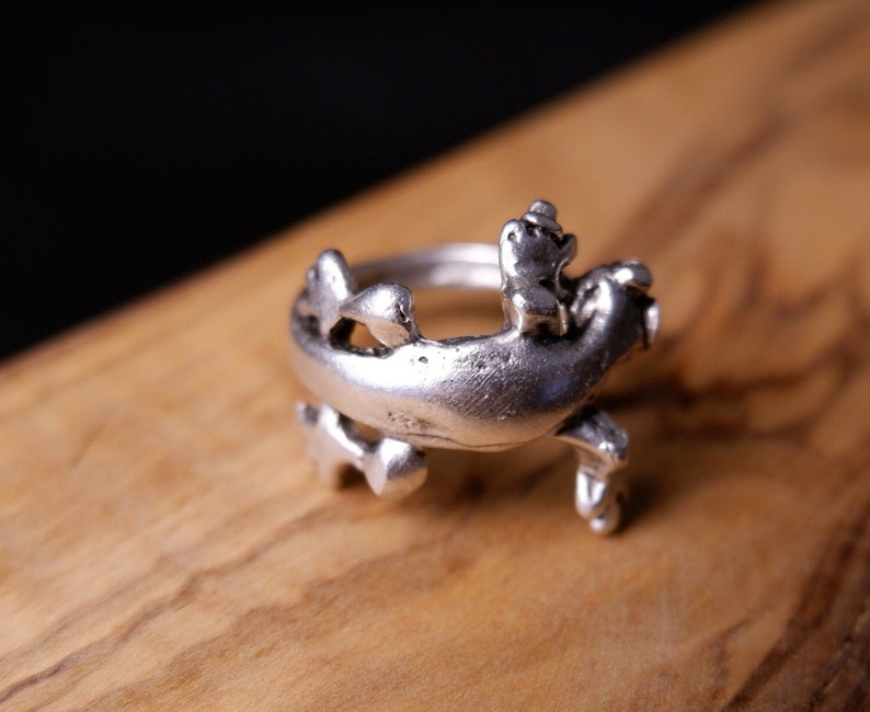 May include: A silver ring with a detailed design of a frog riding another frog.