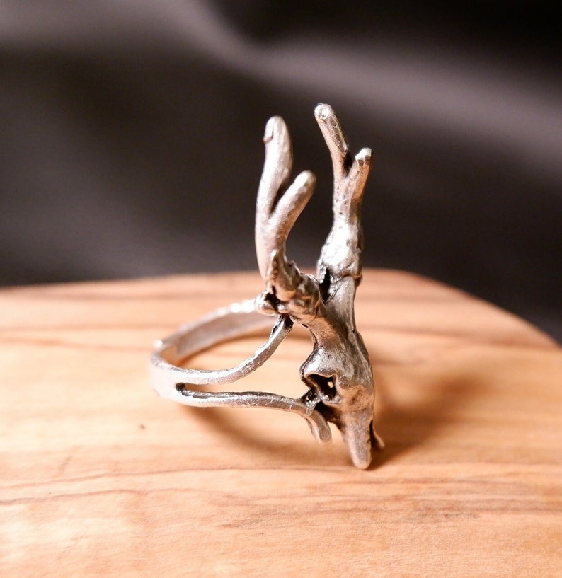 May include: A silver ring with a deer antler design. The ring is made of metal and has a detailed antler design.
