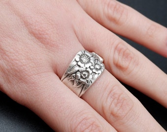 May include: A silver ring with a floral design featuring three flowers with a small clear stone in the center of each flower.