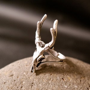 May include: Silver ring with a detailed deer skull design. The ring is open and adjustable.