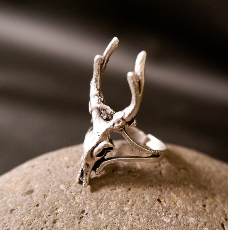 May include: Silver ring with a detailed deer skull design. The ring is open and adjustable.