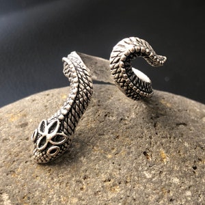 Op de afbeelding: Een zilveren slangenring met een gedetailleerd, gestructureerd ontwerp. De ring is open en wikkelt zich om de vinger.