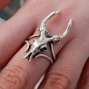 May include: Silver ring featuring a detailed deer skull design with antlers. The ring is adjustable and has a delicate, intricate design.