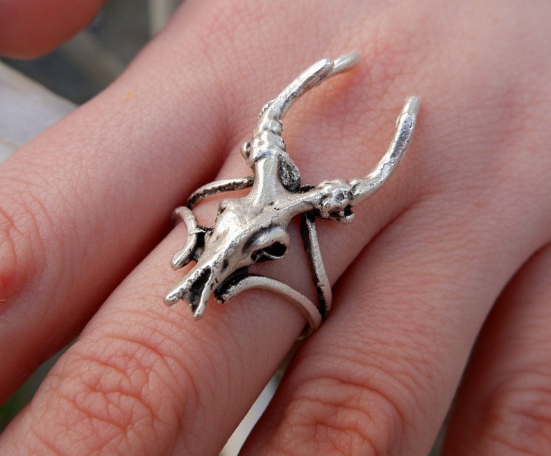 May include: Silver ring featuring a detailed deer skull design with antlers. The ring is adjustable and has a delicate, intricate design.