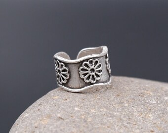 May include: Silver ear cuff with a wavy design and three embossed flower details.