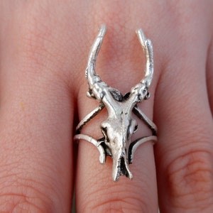 May include: A silver ring featuring a detailed skull with antlers. The ring is designed to fit on the middle finger.