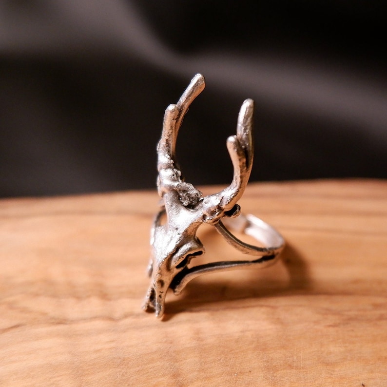 May include: A silver ring with a deer skull design. The ring is open and adjustable.