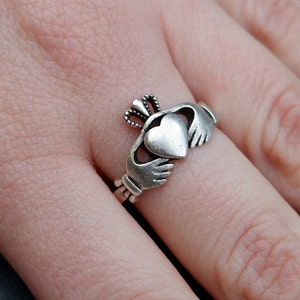 May include: A silver Claddagh ring featuring a heart at its centre, two hands on either side of the heart, and a crown atop the heart.