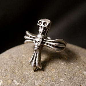 May include: A silver ring with a skull-shaped cross design. The cross has a detailed design with multiple ridges and a skull at the top.