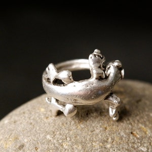 May include: A silver ring with a detailed design of a stylized seahorse. The ring is made of metal and has a smooth finish.