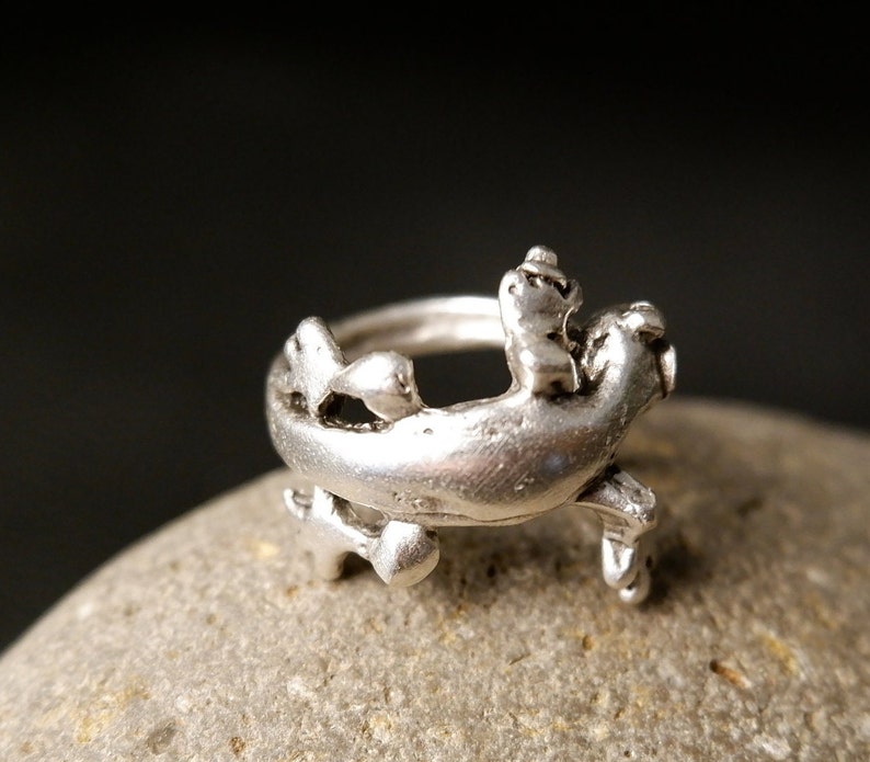 May include: A silver ring with a detailed design of a stylized seahorse. The ring is made of metal and has a smooth finish.