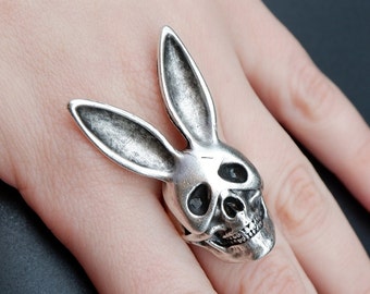 May include: A silver ring featuring a skull with bunny ears. The skull has black eye sockets and a detailed mouth.