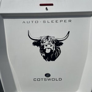Pu&ograve; includere: Un camper bianco con le parole "AUTO-SLEEPER" e "COTSWOLD" in lettere nere. Un'illustrazione in bianco e nero di una mucca delle Highlands con la lingua di fuori &egrave; centrata sul camper.