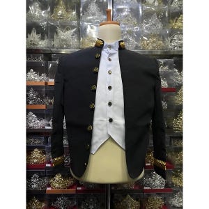 Könnte beinhalten: Ein schwarzer Blazer mit goldenen Verzierungen an Kragen und Ärmeln. Der Blazer wird über einem weißen Hemd und einer weißen Weste getragen.