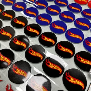 May include: A sheet of assorted Hot Wheels stickers. The stickers are round and feature the Hot Wheels logo in red and yellow on a black, blue, or red background.