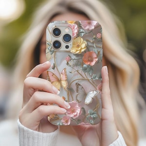 May include: A clear phone case featuring a floral and butterfly design. The case has a 3D effect with pink, yellow, and orange flowers, and two butterflies. The case has a gold-colored border.