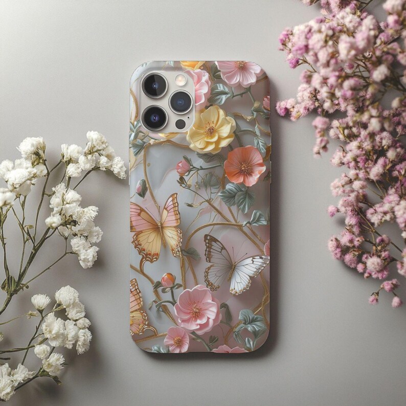 Op de afbeelding: Een telefoonhoesje met een bloemen- en vlinderpatroon. De hoes heeft een lichtgrijze achtergrond met roze, gele en oranje bloemen en vlinders in roze en witte tinten. Het ontwerp bevat goudkleurige wijnranken.