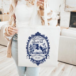 Könnte beinhalten: Weißer Stoffbeutel mit blau-weißem Design. Das Design zeigt den Text "Obstinate Headstrong Girls Book Club" und eine Illustration von Büchern, einer Teekanne und einer Feder. Der Beutel enthält auch den Satz "fiercely independent" und das Jahr "Est. 1813."