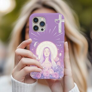 May include: A lavender phone case featuring a religious illustration. The design includes a cross with a heart, a haloed figure, roses, and a celestial background. The case has a protective bumper and camera cutouts.