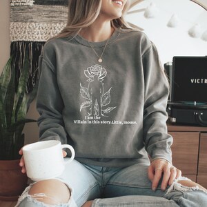 May include: Gray sweatshirt with a white graphic of a rose, a silhouette of a person, and the text "I am the Villain in this story. Little, mouse." The sweatshirt is a crew neck style.
