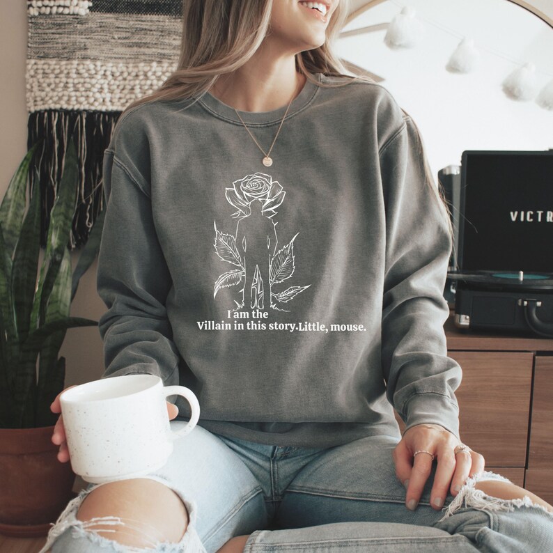 May include: Gray sweatshirt with a white graphic of a rose, a silhouette of a person, and the text "I am the Villain in this story. Little, mouse." The sweatshirt is a crew neck style.