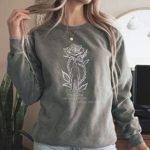 May include: A gray sweatshirt with a white graphic of a rose, a silhouette of a person, and the text "I AM THE VILLAIN IN THIS STORY LITTLE MOUSE". The sweatshirt has long sleeves and a crew neck.