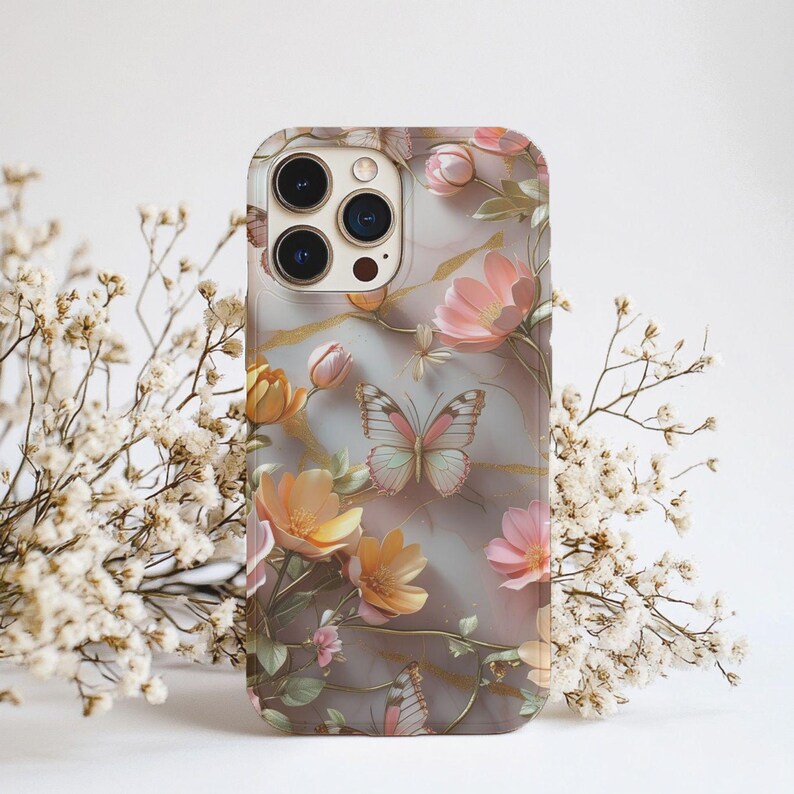 Op de afbeelding: Een telefoonhoesje met een bloemen- en vlinderontwerp. De hoes heeft een transparante achtergrond met roze, perzik en gele bloemen en vlinders. Het ontwerp bevat gouden accenten en een marmerachtige textuur.