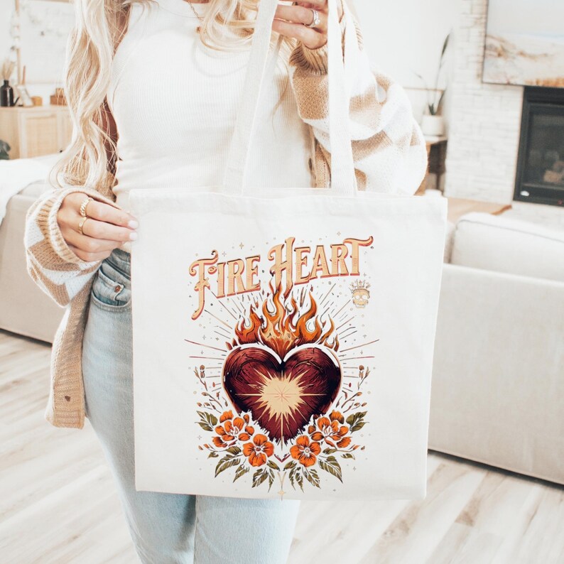 May include: Cream canvas tote bag with a heart design, flames, flowers, and the text "Fire Heart" in orange and brown. The bag has two handles.