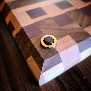 Könnte beinhalten: Nahaufnahme eines Holzschneidebretts mit einem Schachbrettmuster. Das Brett hat einen Fuß aus Messing und schwarzem Gummi an der Unterkante.