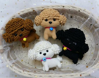 May include: Four crocheted poodle dog toys in a wicker basket. The poodles are brown, white, black, and cream. Each poodle has a small bell attached to its collar.