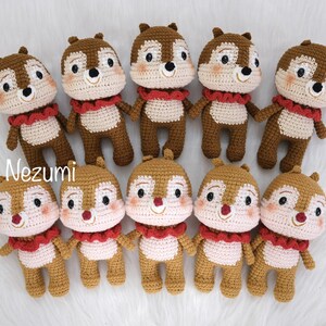 May include: Ten crocheted brown and pink squirrel plushies with red ruffled collars. The plushies are arranged in two rows of five. The plushies have black eyes and a smiling expression.