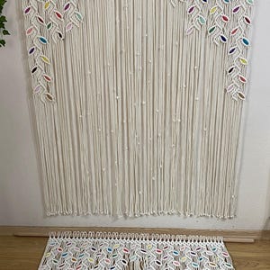 Puede incluir: Un tapiz de macram&eacute; blanco con detalles coloridos. El tapiz presenta un patr&oacute;n de hojas y est&aacute; hecho de cord&oacute;n de algod&oacute;n.