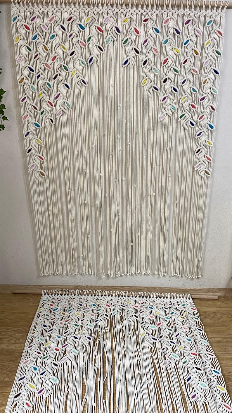 Puede incluir: Un tapiz de macram&eacute; blanco con detalles coloridos. El tapiz presenta un patr&oacute;n de hojas y est&aacute; hecho de cord&oacute;n de algod&oacute;n.