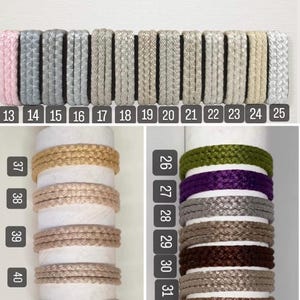 K&ouml;nnte beinhalten: Eine Sammlung von 44 verschiedenen Farben geflochtener Kordel, die auf einem wei&szlig;en Hintergrund und einem Holzstab pr&auml;sentiert werden. Die Kordeln sind von 1 bis 44 nummeriert.