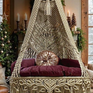 Peut inclure: Un fauteuil suspendu en macramé beige avec un coussin bordeaux et un coussin en sequins dorés. Le fauteuil est doté d'une bordure en franges et est suspendu à un plafond en bois.