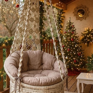 May include: A beige macrame hanging chair with a round, cushioned seat. The chair is suspended from a wooden beam and decorated with tassels. The background features a Christmas tree with red and gold ornaments, and string lights, creating a cozy, festive atmosphere.