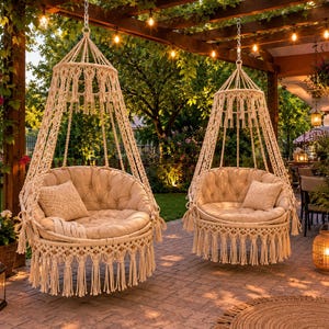 May include: Two hanging macrame chairs with off-white woven rope patterns, circular frames, and long fringe detailing. Each chair features a plush, tufted, off-white circular seat cushion and a matching square throw pillow, suspended by chains.