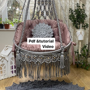 以下が含まれることがあります： グレーの マクラメ ハンギング チェア に、ピンクのベルベット クッション とグレーのクロシェ クッション が付いています。椅子は白い天井から吊り下げられており、床にはグレーのクロシェ ラグ が敷かれています。椅子には「Pdf & tutorial Video」というテキストが表示されています。