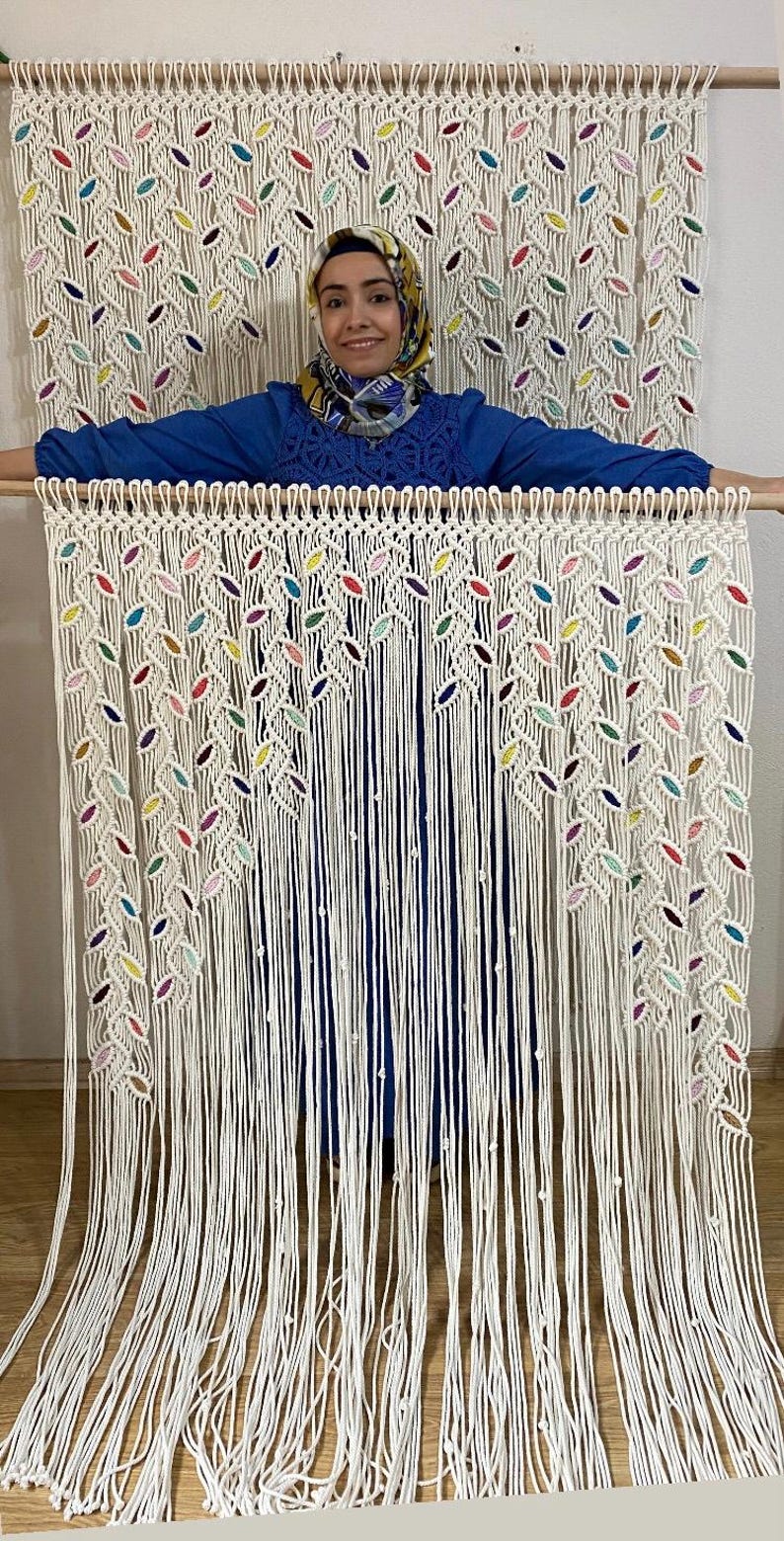 Puede incluir: Un tapiz de macram&eacute; blanco con detalles coloridos. El tapiz presenta un patr&oacute;n de hojas y est&aacute; hecho con cord&oacute;n de algod&oacute;n grueso.