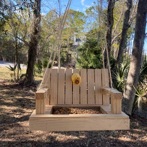 May include: A wooden bird feeder shaped like a hanging swing with a small tray for birdseed. The feeder is hanging from a rope and has a corn cob hanging from the top.