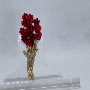 May include: A gold-toned brooch with a bouquet of red flowers. The flowers are made of enamel and have a glossy finish.