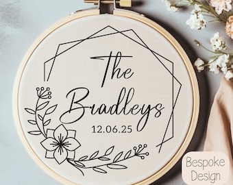May include: A white embroidery hoop with a black geometric frame and floral design. The text "The Bradleys 12.06.25" is inside the frame.