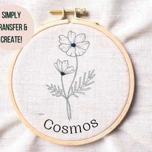 Peut inclure: Un cercle de broderie blanc avec un dessin au trait noir de fleurs de cosmos et le mot "Cosmos" écrit en dessous. Le texte "Simply Transfer & Create!" est écrit dans un cercle rose en haut à gauche.