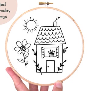 May include: Black and white embroidery design of a house with a flower and sun. The house has a chimney with smoke, a window with a plant, and a door. The design is perfect for hand embroidery projects.