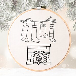 May include: A black and white illustration of a fireplace with stockings hanging from a branch above it. The stockings are decorated with simple patterns.