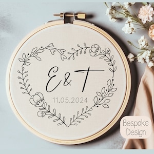 May include: A white embroidery hoop with a black floral design and the initials "E & T" and the date "11.05.2024".